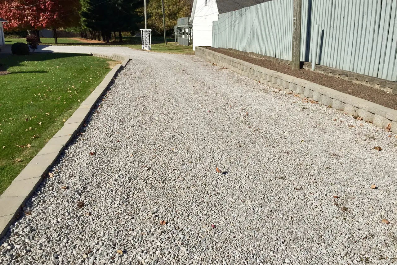 Crushed stone driveway with a block border running beside a fence